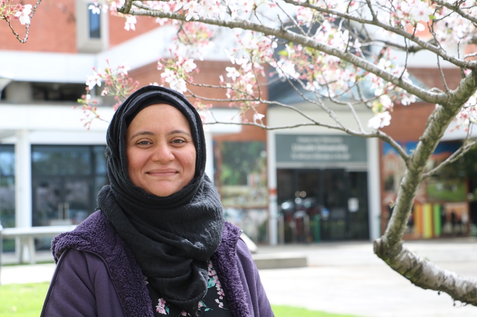 A woman in a hijab smiling in front of a cherry tree