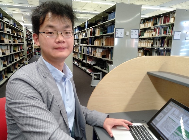 A Chinese man in a suit jacket and business shirt sits using a computer in a library