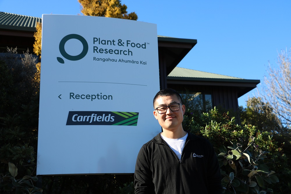 A smiling man standing in front of a sign for Plant and Food Research