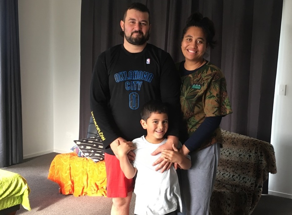 Dad, mum and a young boy stand together in a living room