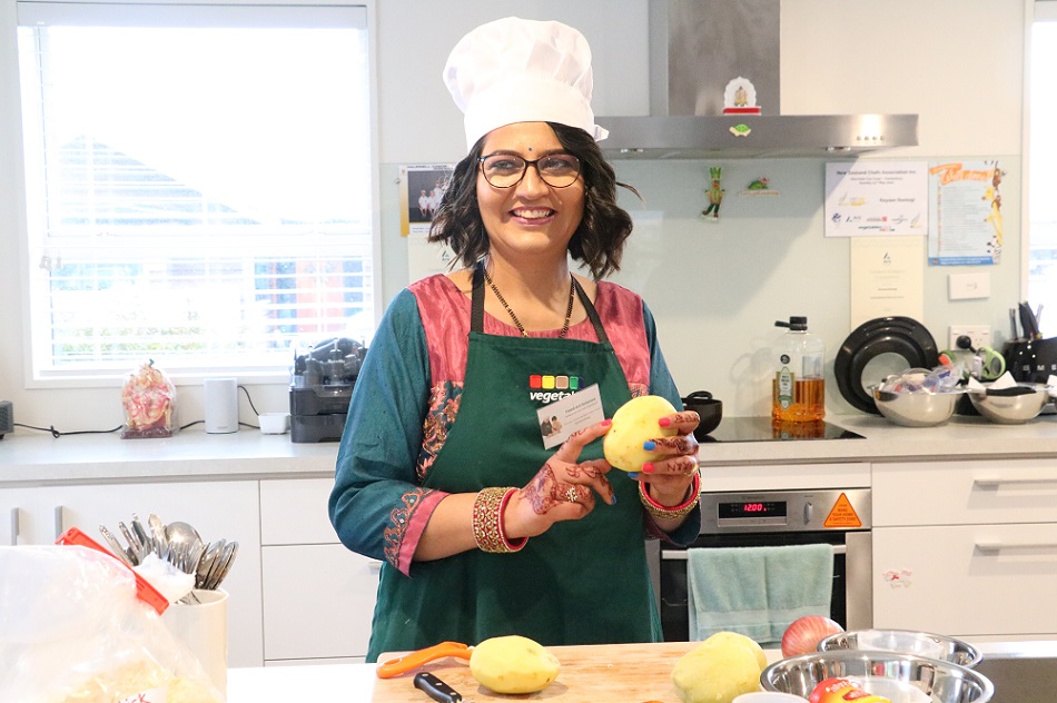 A woman in a home kitchen wearing a chef's hat and pealing a potato