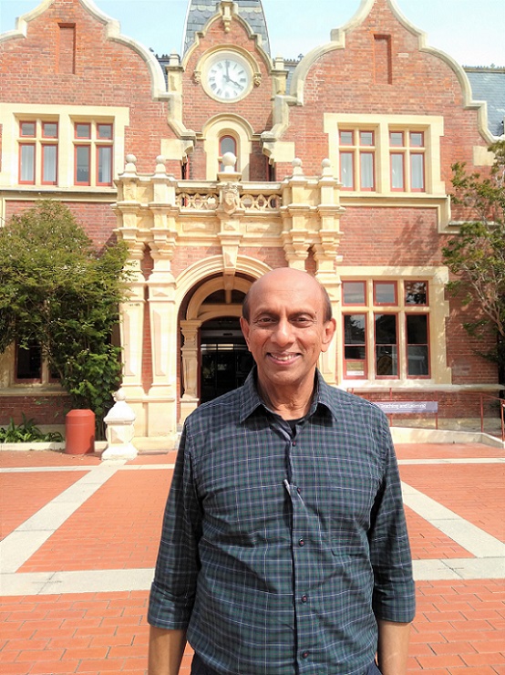 A smiling Sri Lankan man stands in front of a heritage brick building at Lincoln University