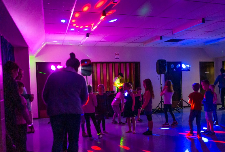 Children dancing at DiscoMania in a hall lit in multi coloured disco lights
