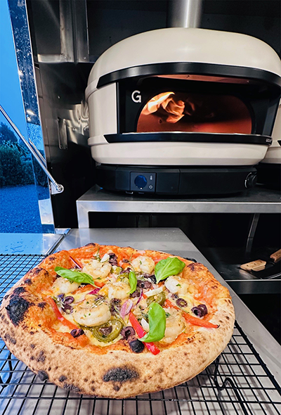 Pizza with array of colourful vegetables in front of pizza oven