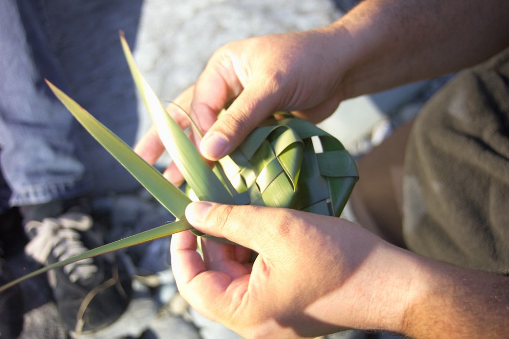 A close up, overhead image of a pair of hands weaving some harakeke