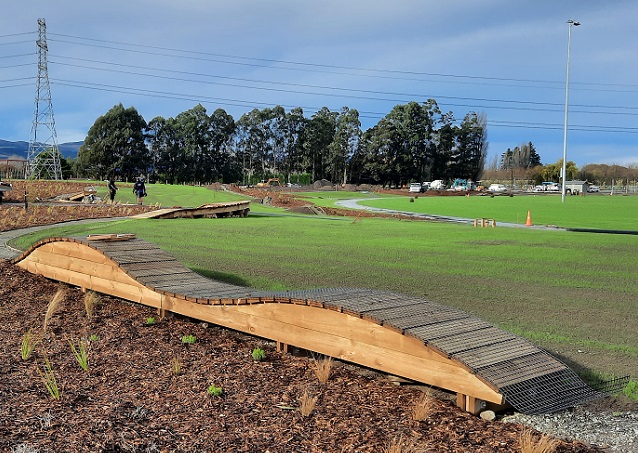 Looking across Kakaha Park shownig a raised undulating wooden bike track along the edge of a grass field