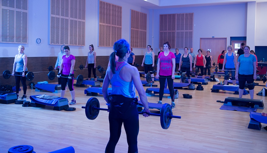 A women's pump class with a group holding weights under purple lights