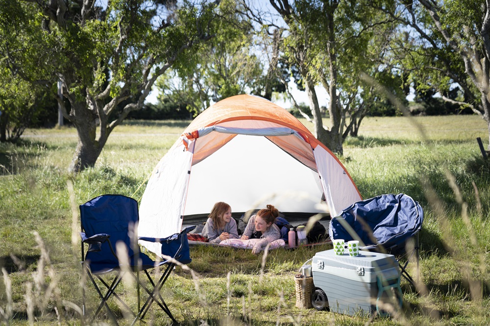 Two children inside a tent camping in a field