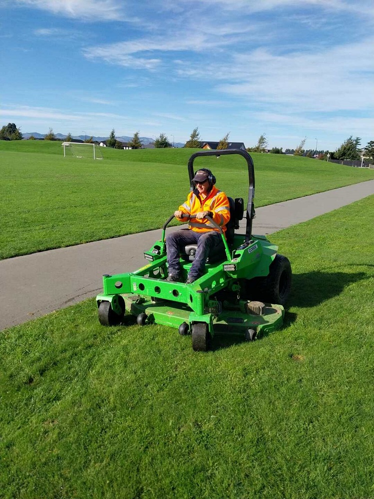 Man in a high visibility jacket sitting on a green ride on lawnmower 