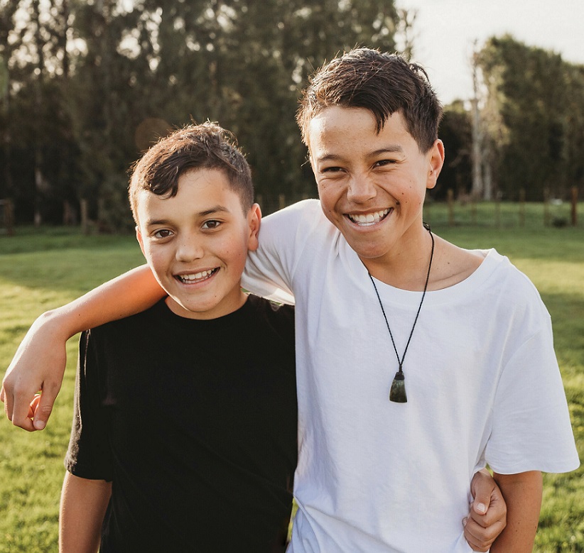 close up of two smiling boys arm in arm in a field