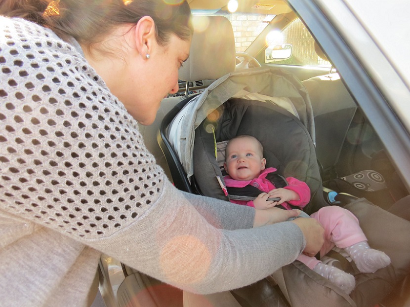 Mum clipping baby into car seat