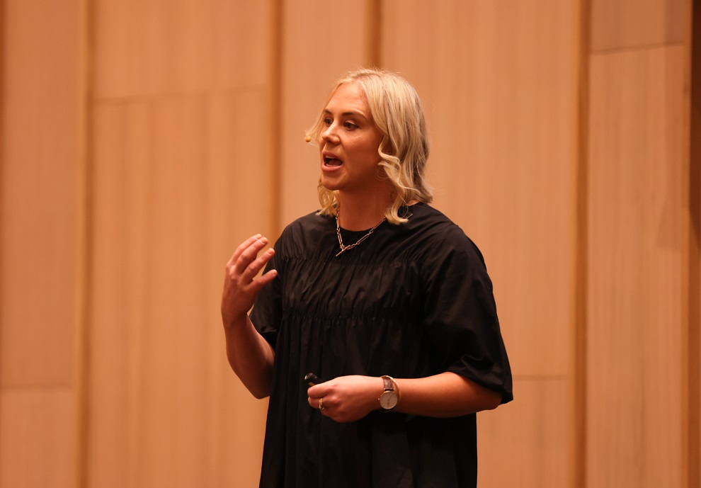 A blonde woman talking on a stage