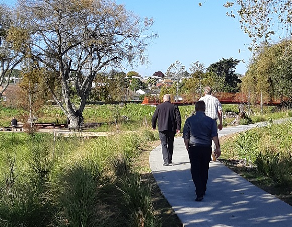 Three men walking away from the camera down a path through a park 