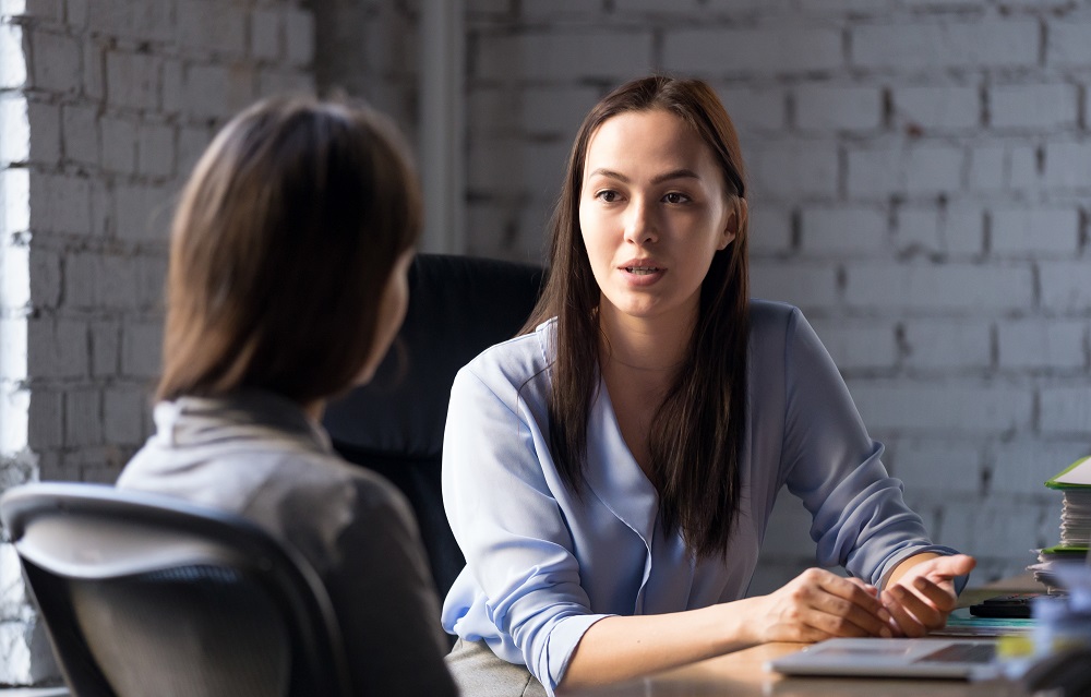 A woman at an office desk talking to another woman
