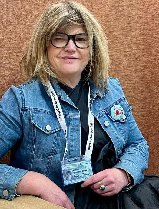 A woman in a blue denim jacket holding out a Hapai Access Card which is on a lanyard round her neck