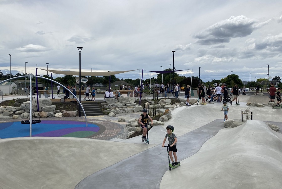 children on scooters in a skate run with crowds round the side