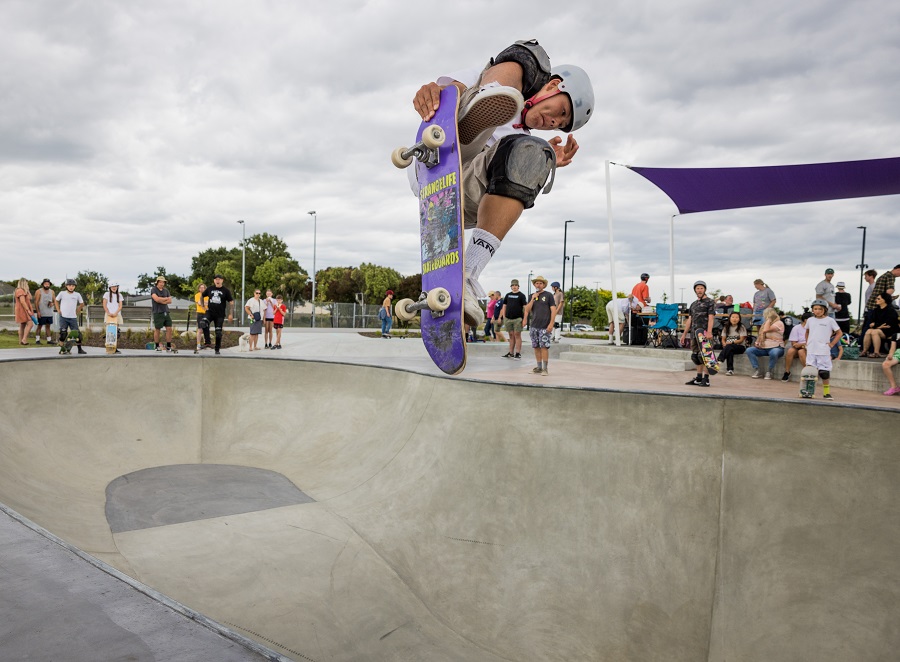A skateboarder in mid air above a skate bowl with a small crowd watching
