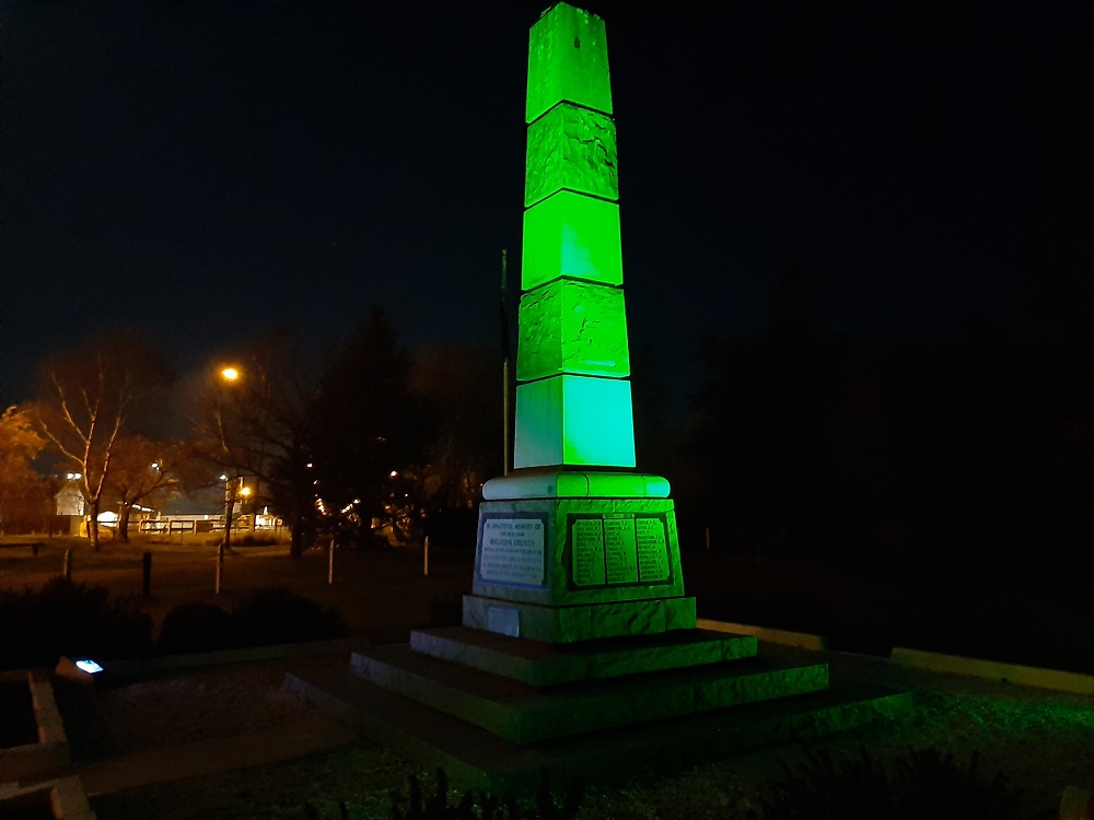 The Darfield War Memorial at night, lit with green light