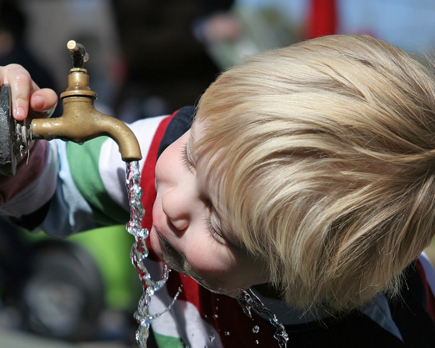 A young boy drinking from a tap