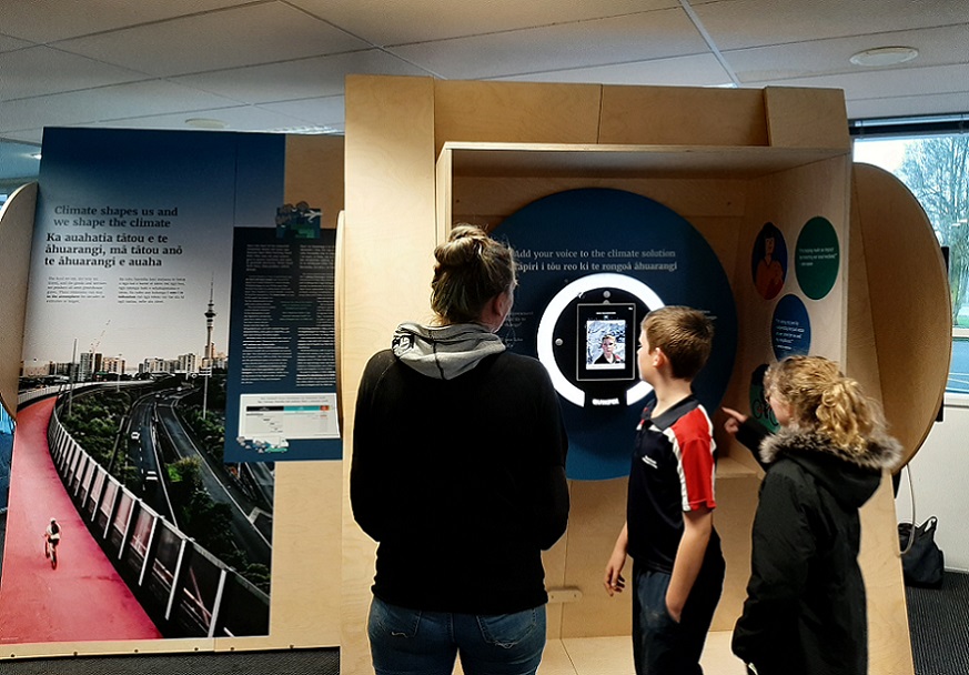 Two children and an adult look at an open photo booth at the exhibition