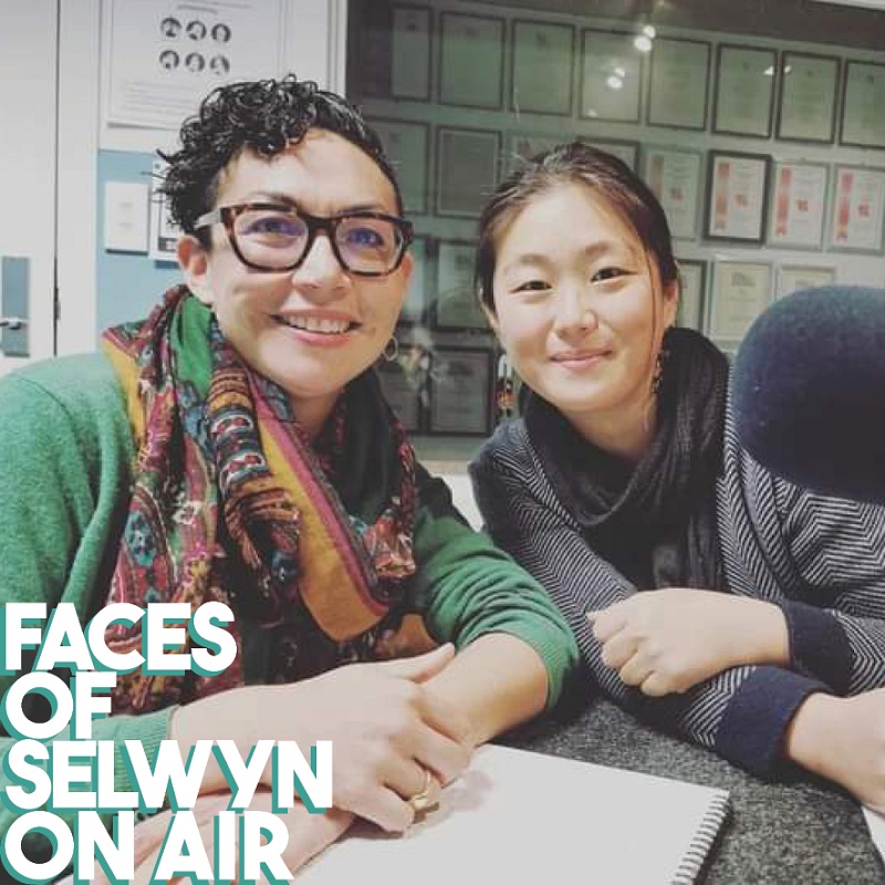 Two women in a radio studio leaning together next to a microphone