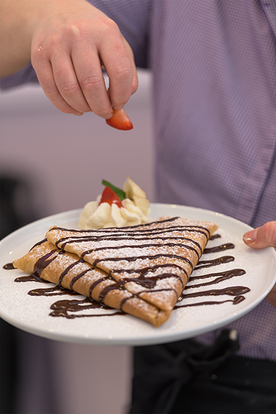 Crepe covered in chocolate nutella spread with a strawberry being places on it