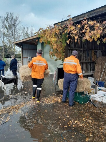 Two people in orange high vis jackets are walking towards a shed