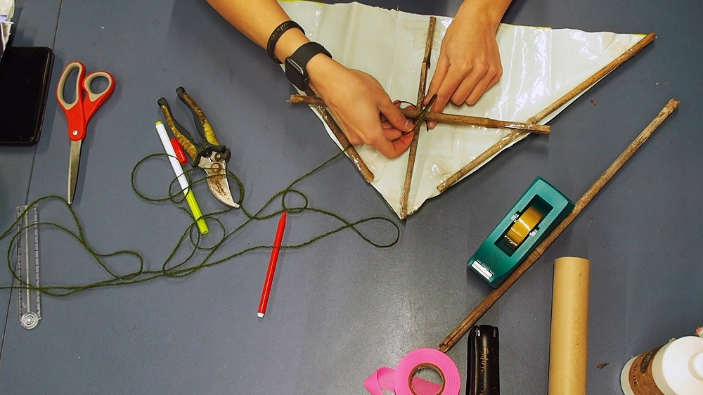 A close up of a pair of hands making a kite, surrounded by craft supplies