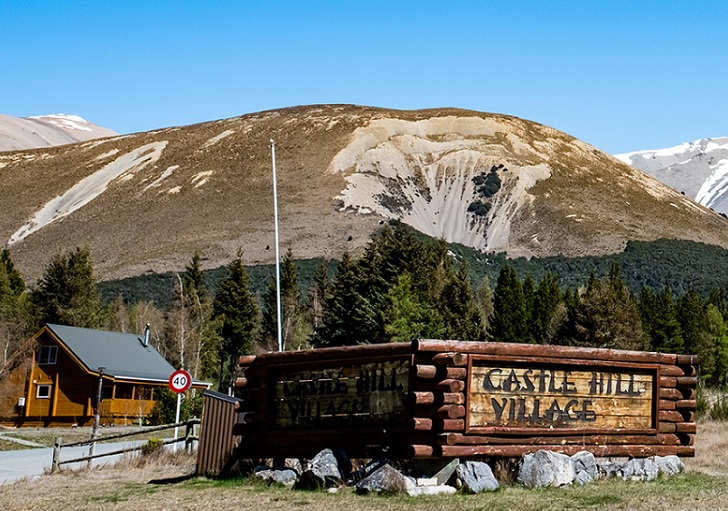 image of square wooden Castle Hill Village sign with a wood house and mountain behind 