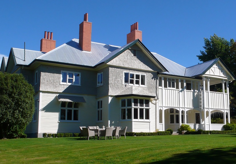 a large wooden heritage house painted grey and white standing surrounded by a green lawn
