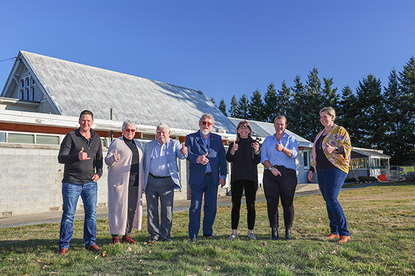 seven people outside hall with thumbs up