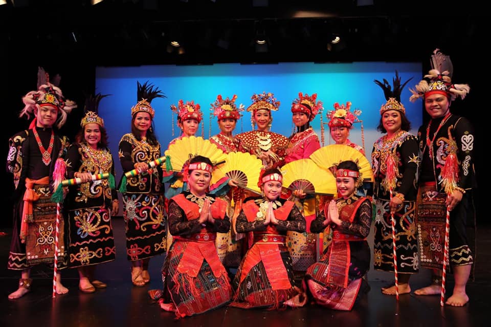 A group of men and women in traditional Indonesian dancing costumes gathered in front of a stage