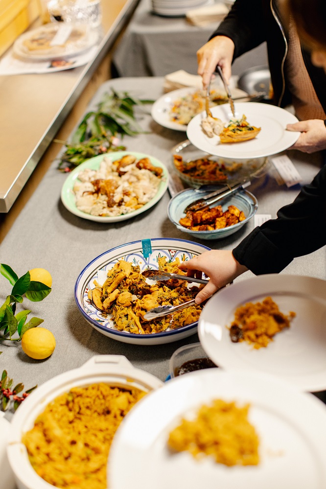 Close up of people selecting food from a table covered in different dishes 