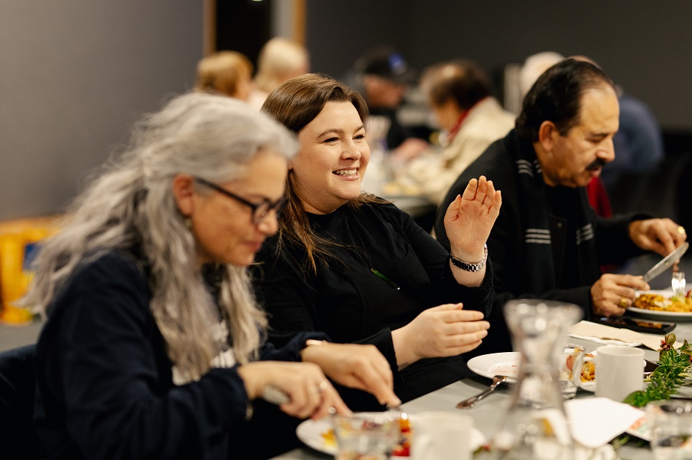 A table of people eating, with a young woman in the centre talking and gesturing with one hand
