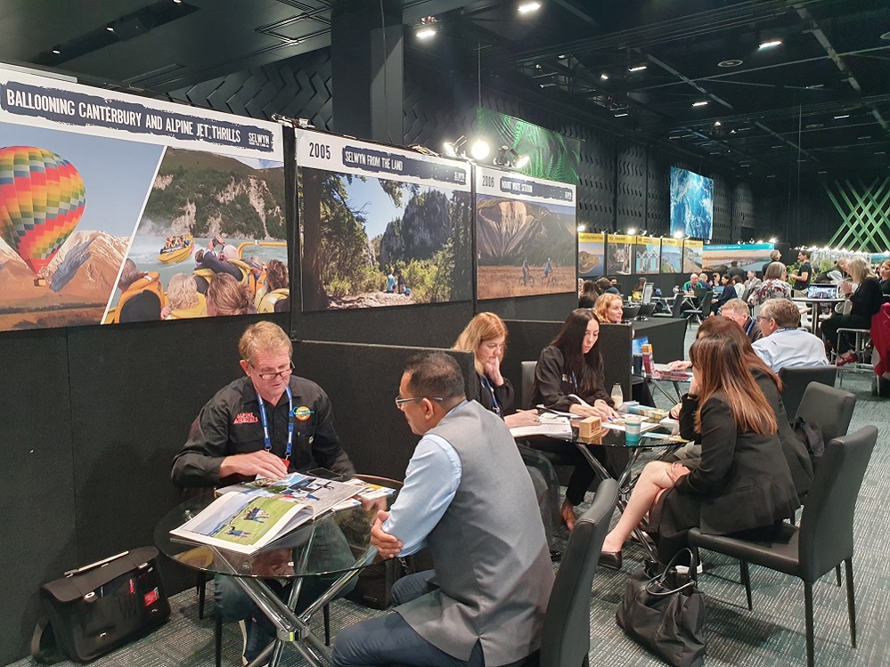 People sitting at tables in a conference hall with posters of images on walls behind her