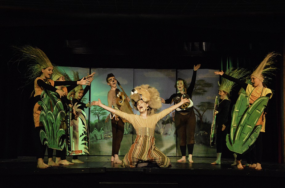 Members of the Kirwee players in costume performing the Lion Kind Jr, with the lion character in the centre on their knees with arms outstretched