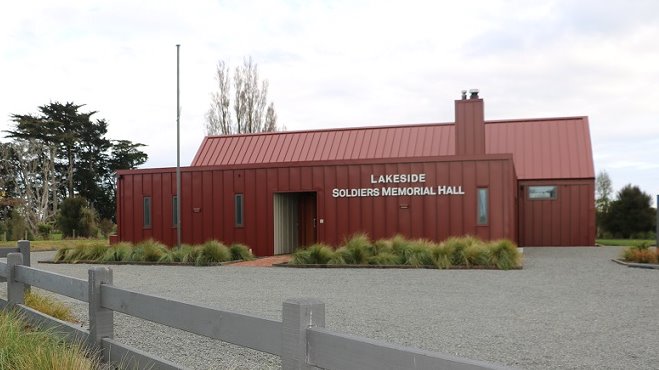 Picture of a square red metal building in front of a barn like red building