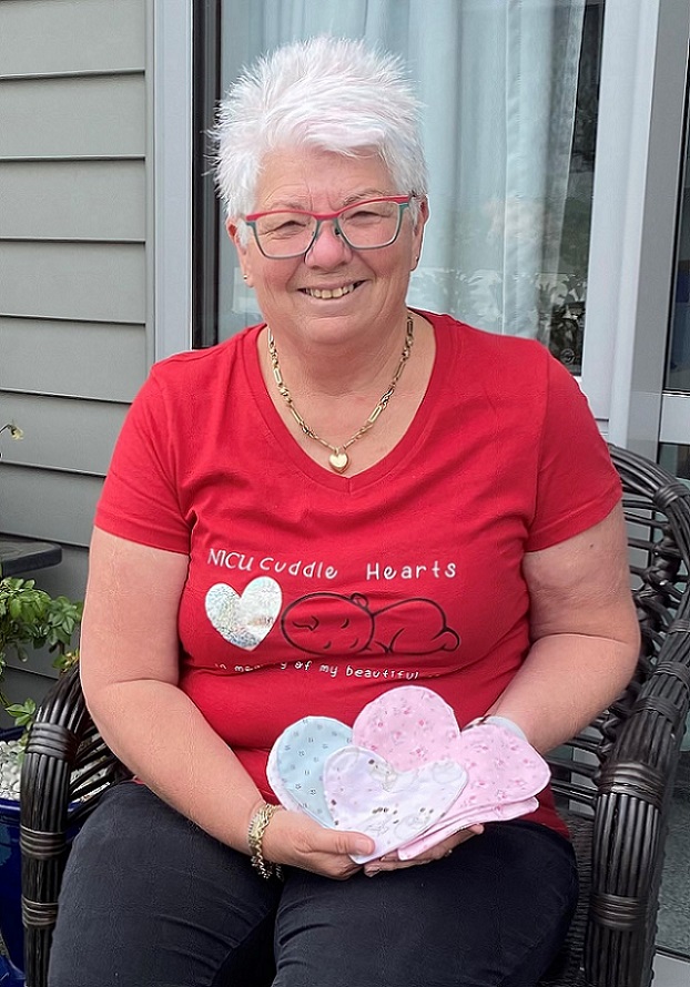 Smiling white haired woman sitting in a wicker chair holding a collection of brightly coloured fabric hearts