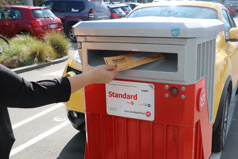 A person puts an orange voting envelope into a post box