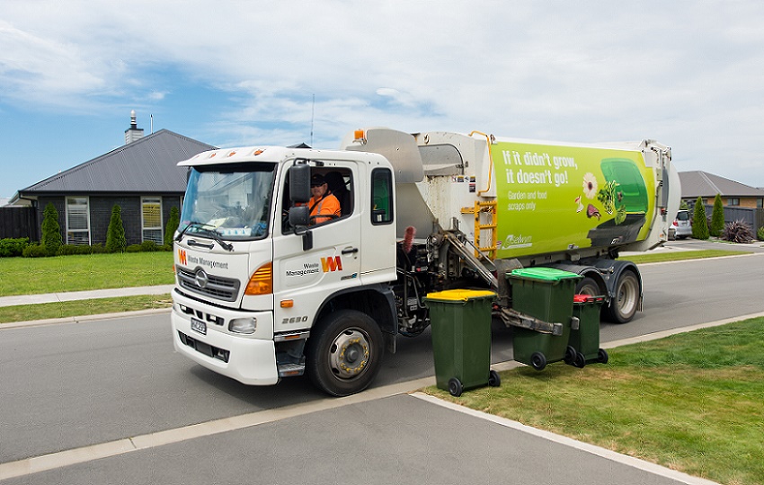 A rubbish truck on a suburban street lifting a green organics bin