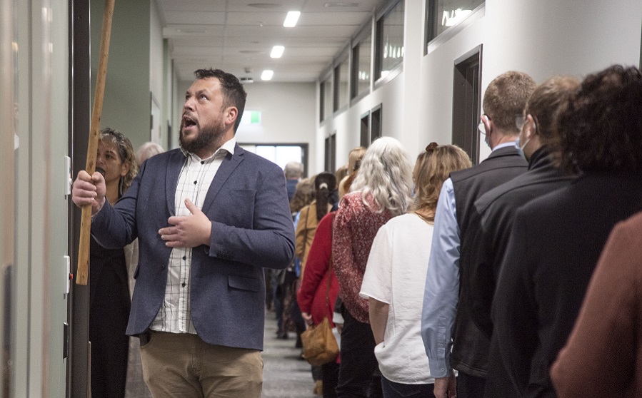 Ngāi Te Ruahikihiki ki Taumutu representative Corban Te Aika holds up a staff while speaking leading a line of people through the inside of the health hub