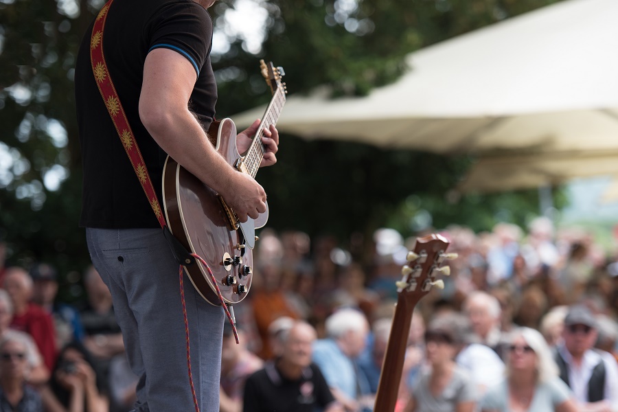 Close up side shot of a person in a black top playing a guitar with a crowd in the background