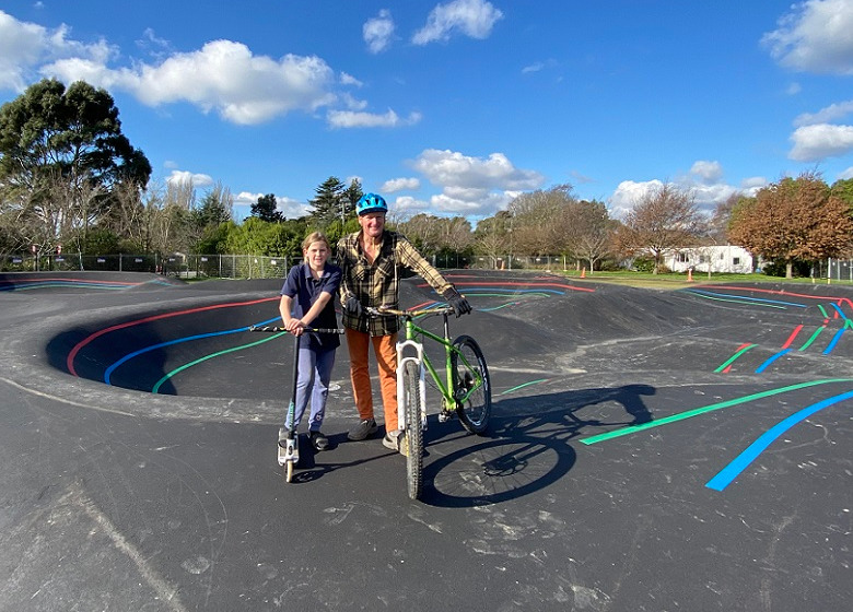 Dad with a bike and daughter with a scooter pose at the edge of the Prebbleton Pump Track