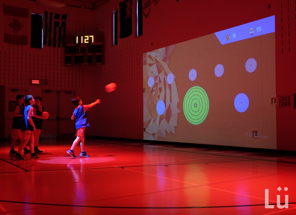 Children throw a ball at a target on a wall in a gym filled with red light