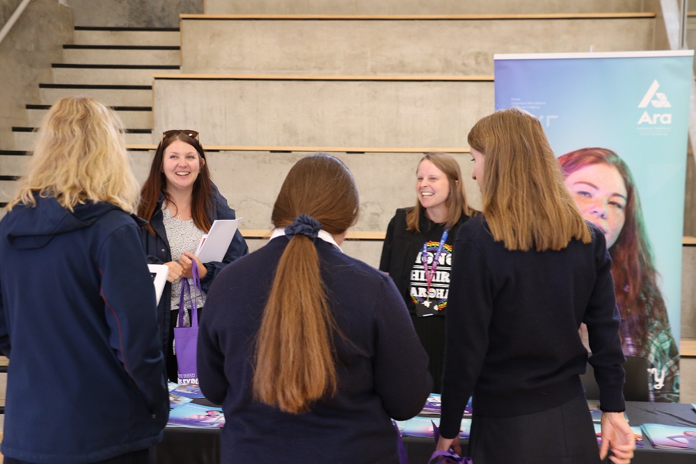 Three students talking to two staff from Ara Institute of Technology at the youth expo