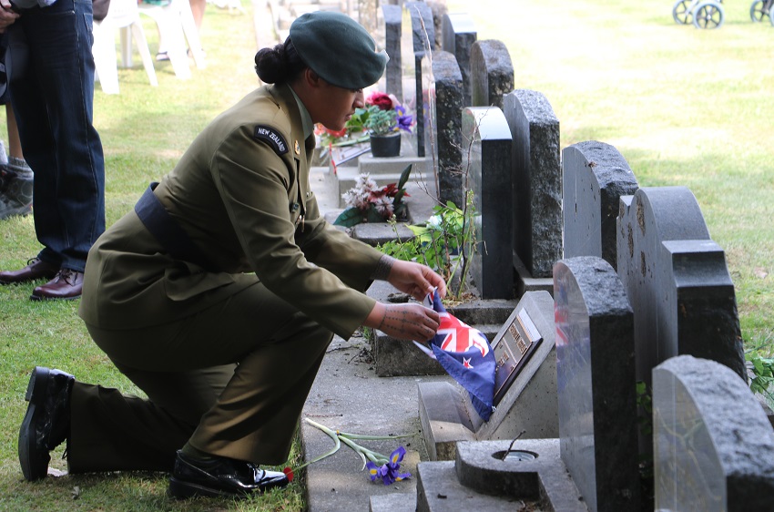 A female soldier in a dress uniform kneels and removes the flag from a plaque