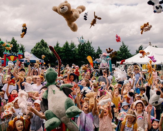 Crowd of smiling children throwing teddy bears in the air