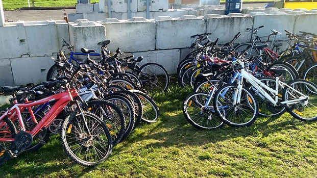 A group of 30 bikes standing on grass and lent against a low breeze block wall