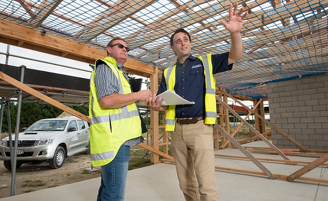 Two men in hi-viz jackets talk inside a half-built building, one pointing
