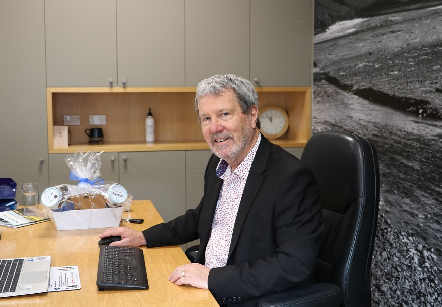 An older David Ward sitting at his desk on his last day